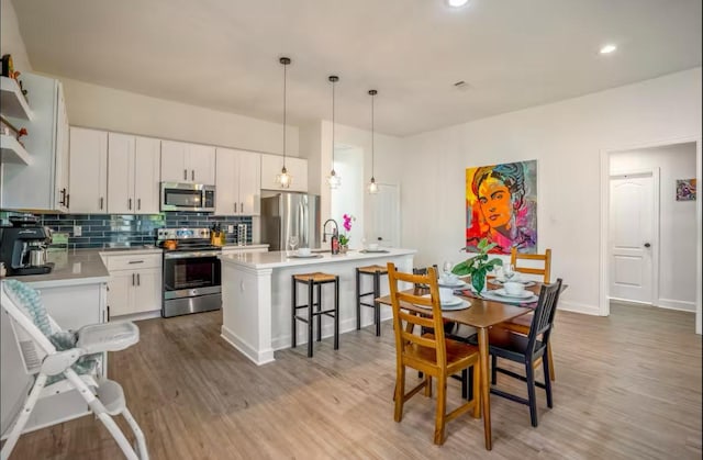 4111 Engelke St, Houston, TX 77003 - kitchen featuring appliances with stainless steel finishes, wood finished floors, light countertops, backsplash, and a center island with sink
