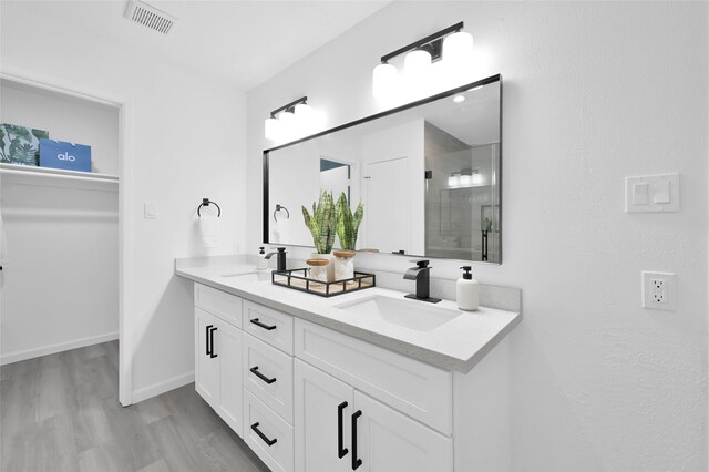 bathroom featuring wood finished floors, a stall shower, double vanity, baseboards, and a walk in closet