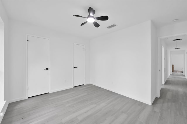 unfurnished bedroom with light wood finished floors, attic access, baseboards, and a ceiling fan