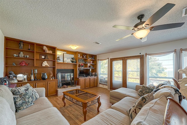 220 Hillcrest Dr, Coldspring, TX 77331 - living room with a textured ceiling, a ceiling fan, light wood-style flooring, and a glass covered fireplace