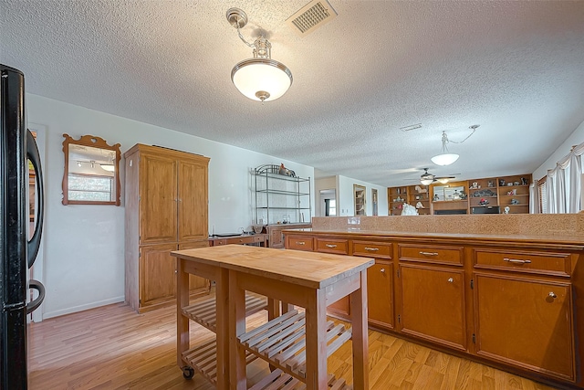 220 Hillcrest Dr, Coldspring, TX 77331 - kitchen featuring freestanding refrigerator, light wood-style floors, brown cabinetry, a textured ceiling, and healthy amount of natural light