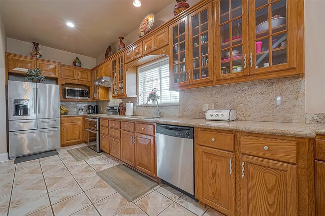 1241 Terrazas Ln, Sealy, TX 77474 - kitchen with appliances with stainless steel finishes, a sink, glass insert cabinets, brown cabinetry, and backsplash