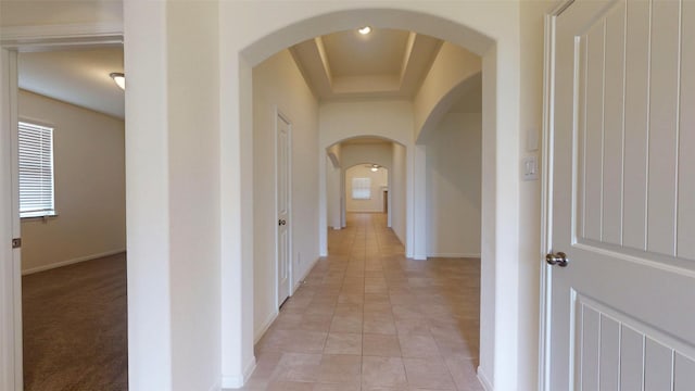 32307 Elmwood Mnr, Waller, TX 77484 - hallway featuring baseboards, arched walkways, light tile patterned floors, and a tray ceiling