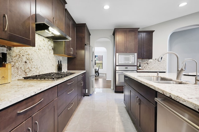 6706 Miller Shadow Ln, Sugar Land, TX 77479 - kitchen with appliances with stainless steel finishes, arched walkways, under cabinet range hood, a sink, and light stone counters