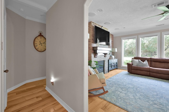 living room featuring a fireplace, light wood-type flooring, a ceiling fan, baseboards, and crown molding