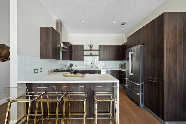 1211 Caroline St Unit 908, Houston, TX 77002 - kitchen featuring appliances with stainless steel finishes, wall chimney exhaust hood, a peninsula, modern cabinets, and a textured ceiling