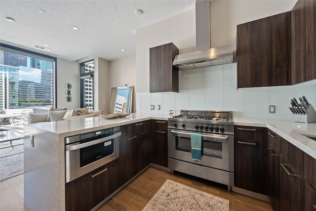 1211 Caroline St Unit 908, Houston, TX 77002 - kitchen with appliances with stainless steel finishes, wall chimney range hood, dark brown cabinets, a textured ceiling, and recessed lighting