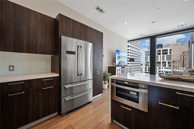 1211 Caroline St Unit 908, Houston, TX 77002 - kitchen with stainless steel appliances, light wood finished floors, dark brown cabinetry, light countertops, and backsplash