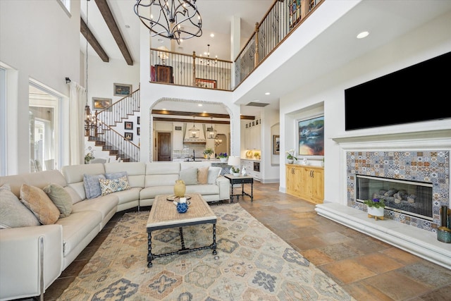 living area with a high ceiling, stairway, stone tile floors, a tiled fireplace, and a chandelier