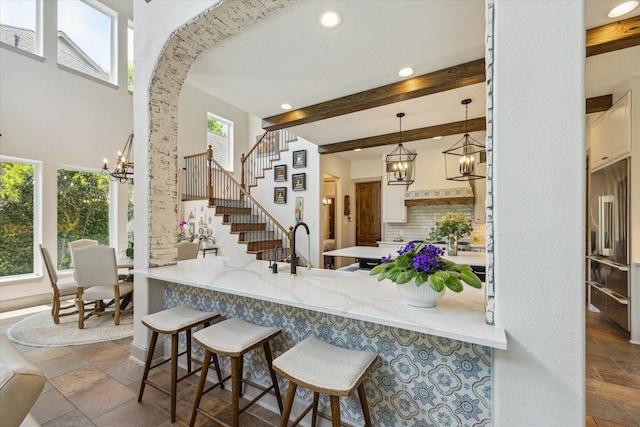 kitchen featuring a chandelier, stone tile flooring, high quality fridge, a peninsula, and recessed lighting