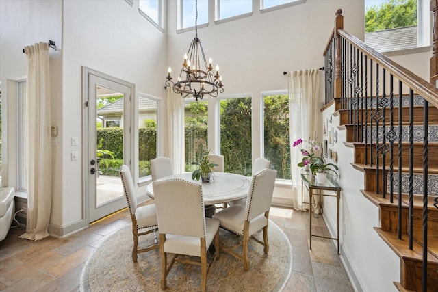 dining space featuring stone tile floors, a towering ceiling, a chandelier, baseboards, and stairs