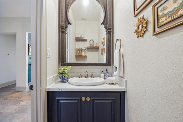 bathroom featuring vanity, stone finish flooring, a textured wall, and baseboards