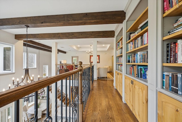 hall featuring a chandelier, wood finished floors, an upstairs landing, beamed ceiling, and a raised ceiling