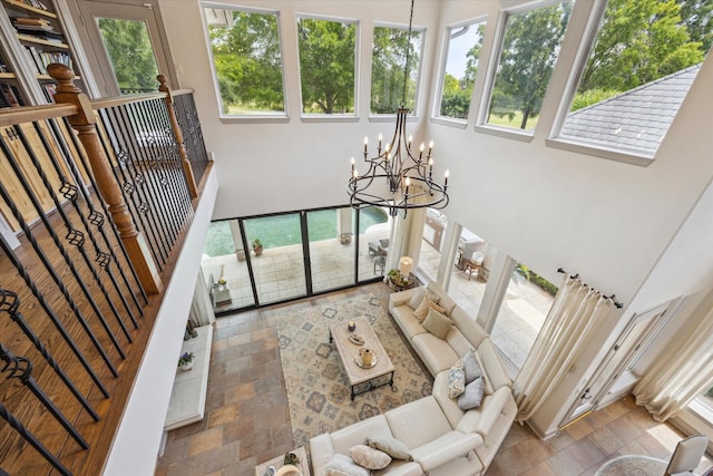 living area featuring a chandelier, a towering ceiling, healthy amount of natural light, and stone finish flooring