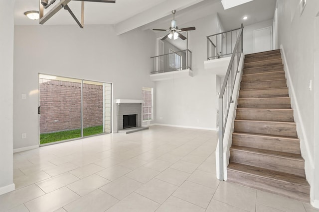 stairs featuring high vaulted ceiling, a ceiling fan, a fireplace with raised hearth, baseboards, and tile patterned floors