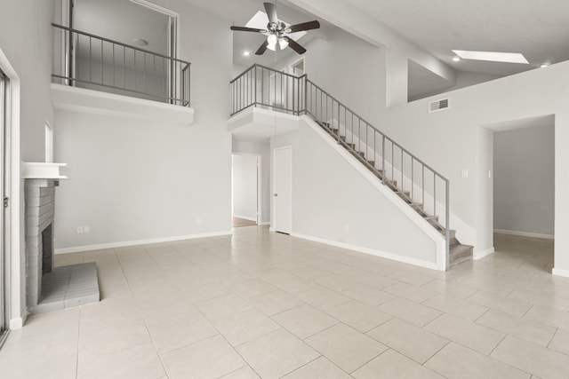 unfurnished living room with high vaulted ceiling, a ceiling fan, stairs, tile patterned floors, and a brick fireplace