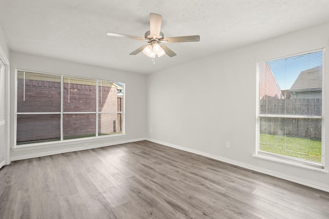 unfurnished room featuring wood finished floors, healthy amount of natural light, baseboards, and ceiling fan
