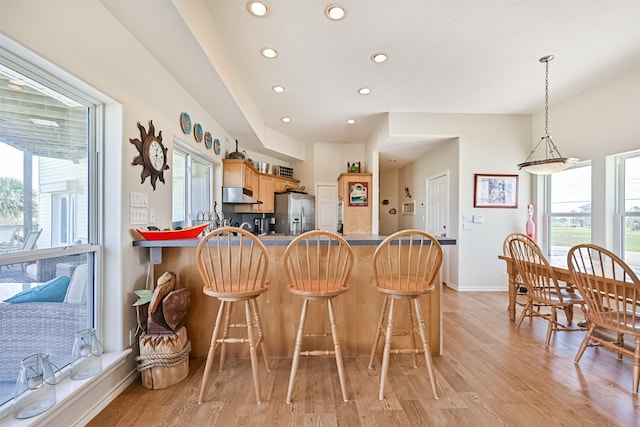 kitchen featuring under cabinet range hood, recessed lighting, stainless steel fridge with ice dispenser, healthy amount of natural light, and light wood-type flooring
