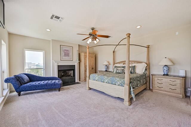 bedroom with light colored carpet, a ceiling fan, a tiled fireplace, and recessed lighting