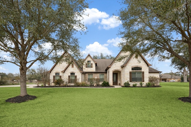 french country home with stone siding, a front lawn, and roof with shingles