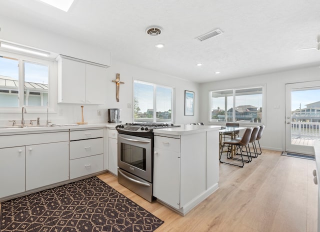 4209 W Bayside Way, Jamaica Beach, TX 77554 - kitchen featuring gas stove, a sink, a peninsula, light wood-style flooring, and white cabinets
