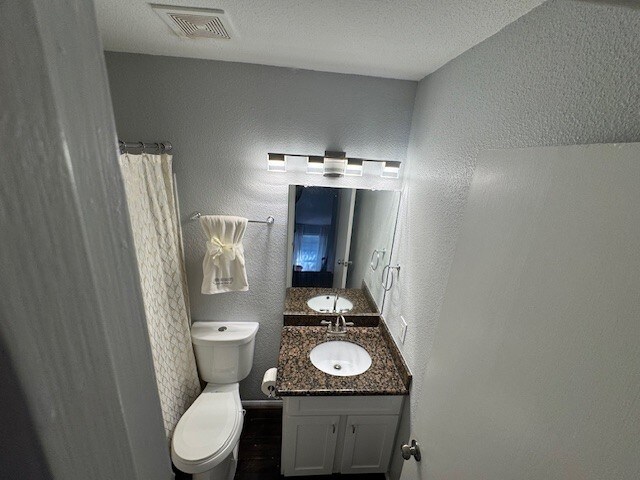 2211 S Kirkwood Rd Unit 1, Houston, TX 77077 - full bath featuring vanity, toilet, a textured wall, a shower with shower curtain, and wood finished floors