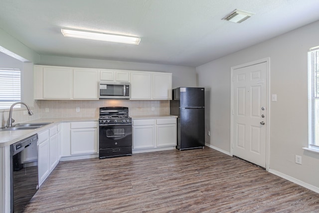 21002 Brannon Hill Ln, Humble, TX 77338 - kitchen with black appliances, a sink, dark wood finished floors, decorative backsplash, and white cabinets