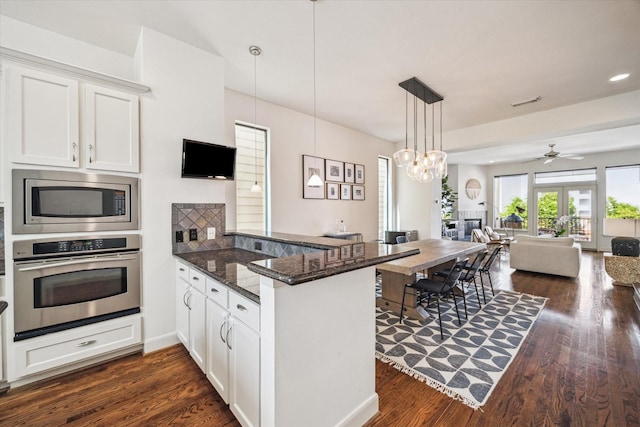 kitchen with stainless steel appliances, a peninsula, white cabinetry, open floor plan, and dark stone counters