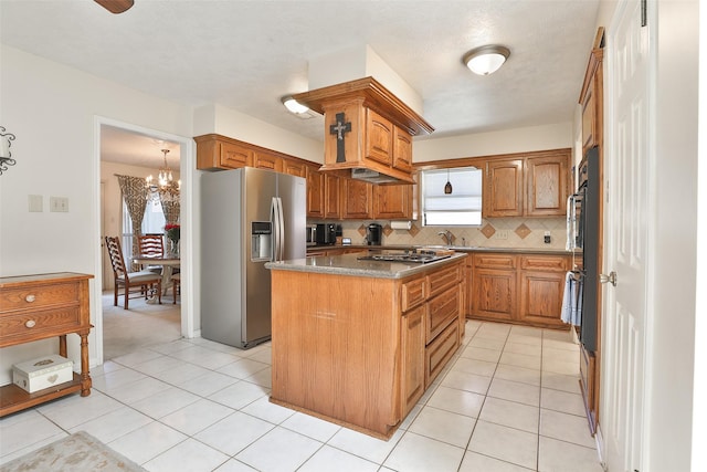 kitchen with appliances with stainless steel finishes, a kitchen island, decorative backsplash, a chandelier, and brown cabinets