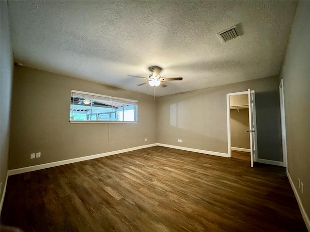 unfurnished bedroom with dark wood-type flooring, a textured ceiling, baseboards, a spacious closet, and ceiling fan
