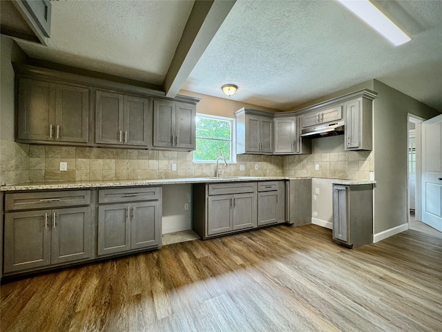 kitchen with gray cabinets, under cabinet range hood, wood finished floors, a textured ceiling, and backsplash