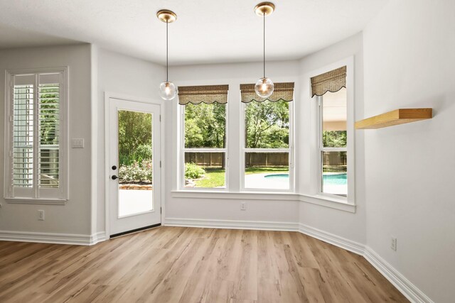 unfurnished dining area featuring light wood-type flooring, healthy amount of natural light, and baseboards