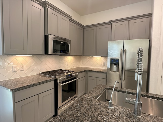 130 Moon Dance Ct, Conroe, TX 77304 - kitchen with stainless steel appliances, gray cabinetry, dark stone countertops, and decorative backsplash
