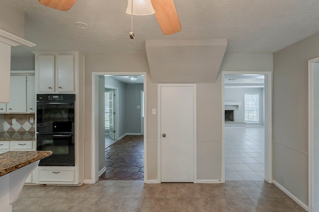 7803 Hurst Forest Dr, Humble, TX 77346 - kitchen featuring white cabinets, tasteful backsplash, light tile patterned floors, dark stone countertops, and a textured ceiling