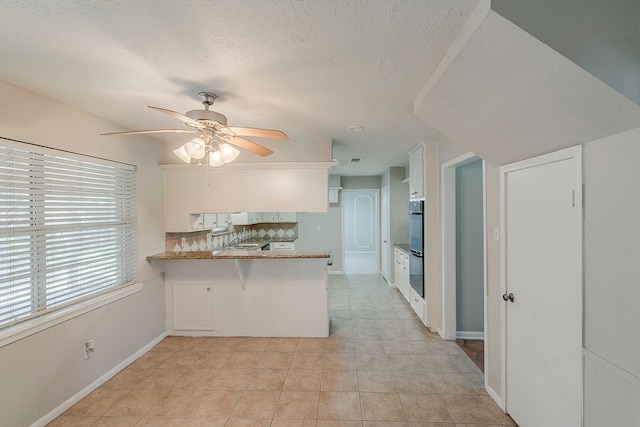 7803 Hurst Forest Dr, Humble, TX 77346 - kitchen featuring ceiling fan, white cabinetry, decorative backsplash, a peninsula, and a textured ceiling