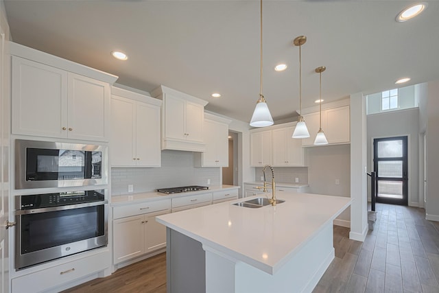 11430 Bush Clover Dr, Cypress, TX 77433 - kitchen with appliances with stainless steel finishes, a sink, decorative backsplash, wood finished floors, and an island with sink