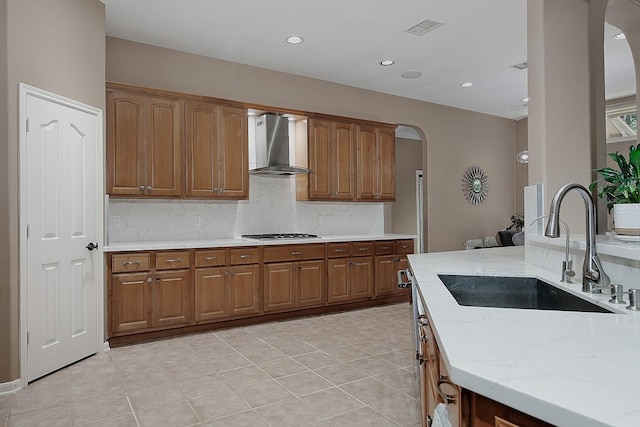 87 S Bluff Creek Cir, The Woodlands, TX 77382 - kitchen featuring wall chimney range hood, a sink, arched walkways, brown cabinets, and decorative backsplash
