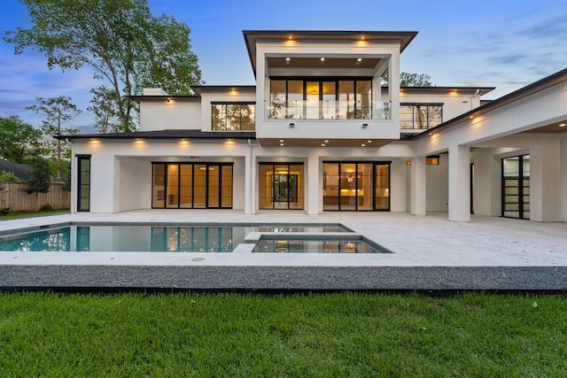 back of property with a balcony, stucco siding, an in-ground hot tub, a patio, and fence