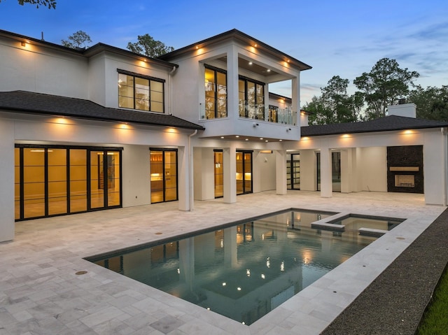 rear view of house with a balcony, a patio area, a pool with connected hot tub, stucco siding, and a chimney