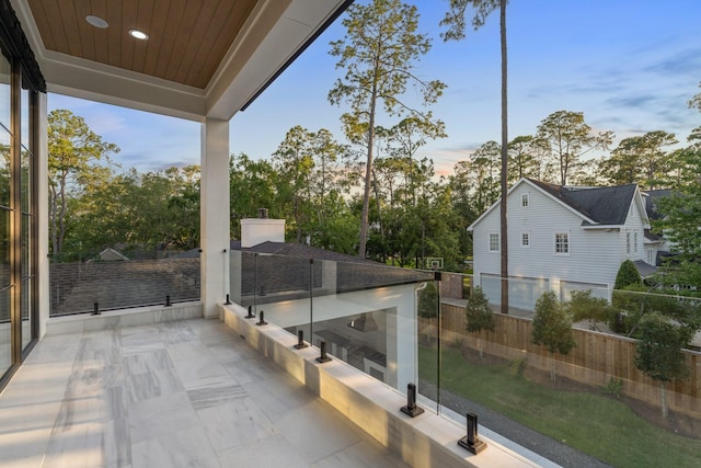 patio terrace at dusk featuring fence and view of wooded area