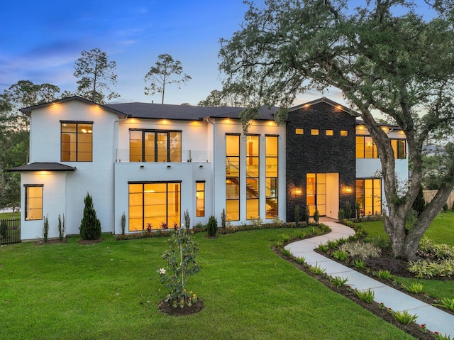 back of property at dusk featuring a yard, stucco siding, and stone siding