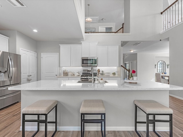 711 Summer Trace Ln, Richmond, TX 77406 - kitchen with stainless steel appliances, a sink, white cabinets, a kitchen breakfast bar, and a towering ceiling