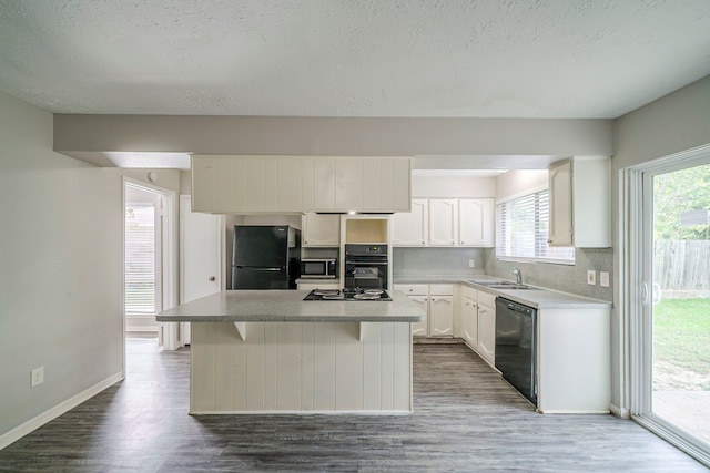 7218 Winding Trace Dr, Houston, TX 77086 - kitchen featuring black appliances, dark wood-style flooring, white cabinets, a center island, and a textured ceiling