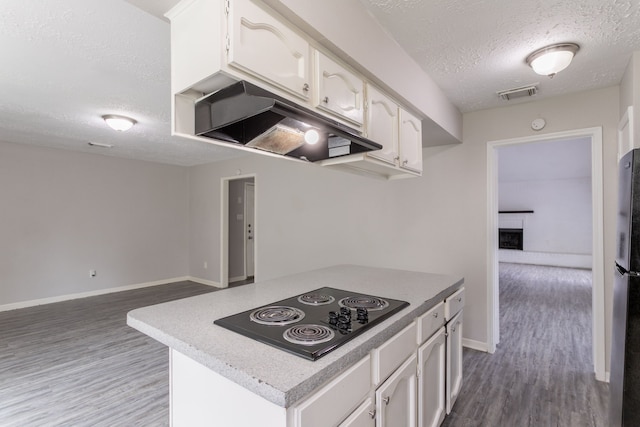 7218 Winding Trace Dr, Houston, TX 77086 - kitchen with black electric stovetop, a textured ceiling, under cabinet range hood, dark wood-type flooring, and white cabinetry