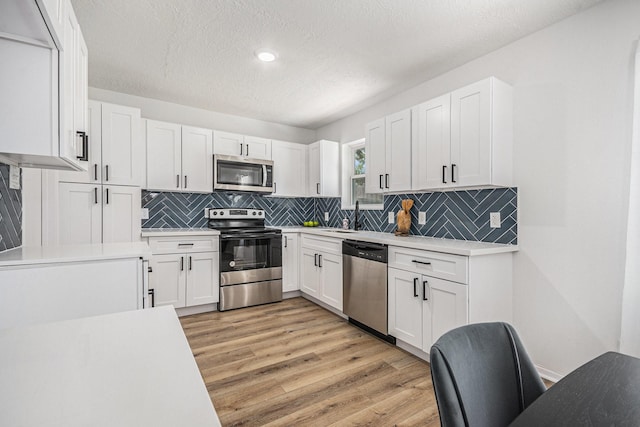 763 Voyager Dr, Houston, TX 77062 - kitchen with appliances with stainless steel finishes, light countertops, a textured ceiling, light wood-style floors, and white cabinetry