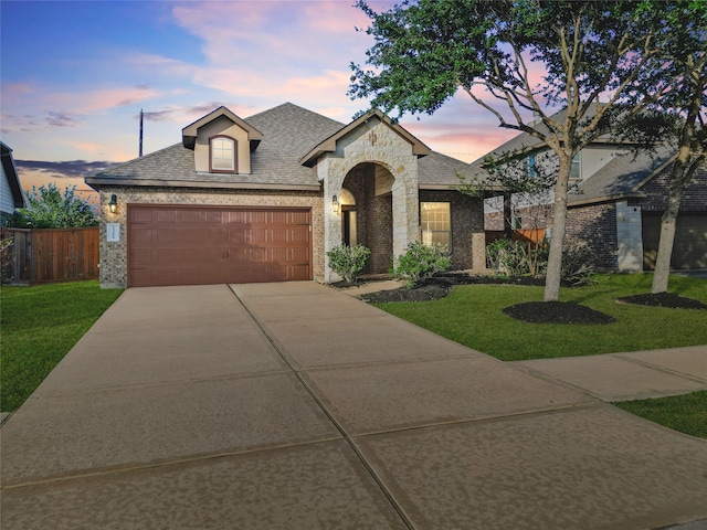 french country inspired facade with brick siding, driveway, a garage, a shingled roof, and stone siding