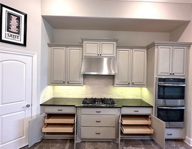 2308 Ellis Park Ln, Conroe, TX 77304 - kitchen with double oven, gas cooktop, under cabinet range hood, dark countertops, and tasteful backsplash