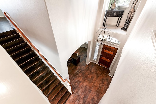staircase featuring wood finished floors, arched walkways, and a chandelier