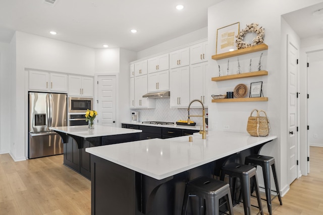 30246 Gold Finch Pl, Fulshear, TX 77441 - kitchen with appliances with stainless steel finishes, under cabinet range hood, a breakfast bar, light countertops, and white cabinets