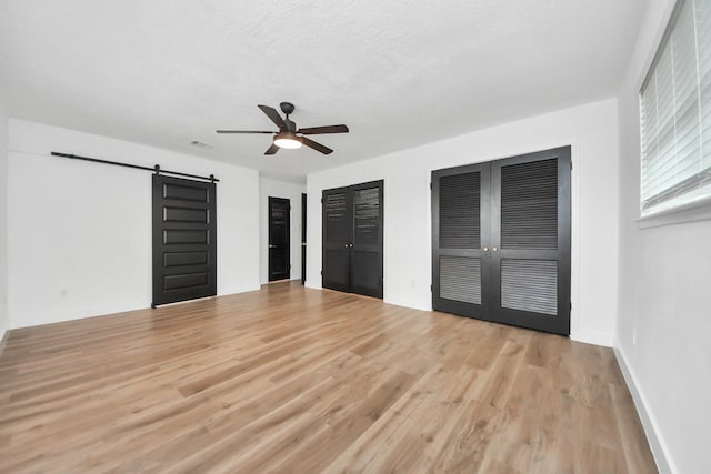 5638 N Braeswood Blvd, Houston, TX 77096 - unfurnished bedroom with a barn door, light wood-type flooring, two closets, a ceiling fan, and baseboards